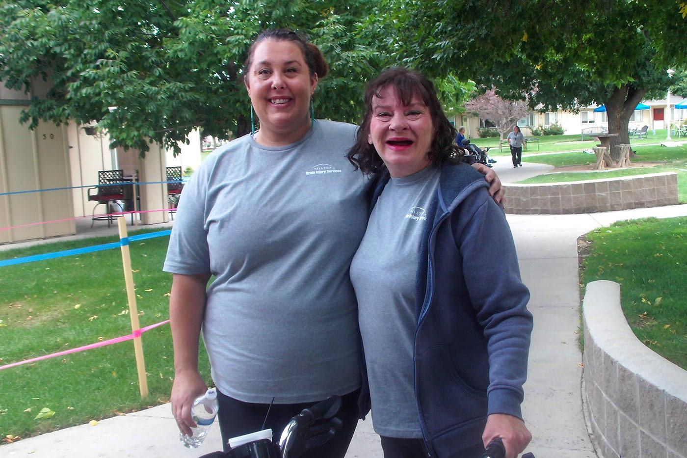 Hilltop Brain Injury Services staff member and resident smiling together outdoors on campus.