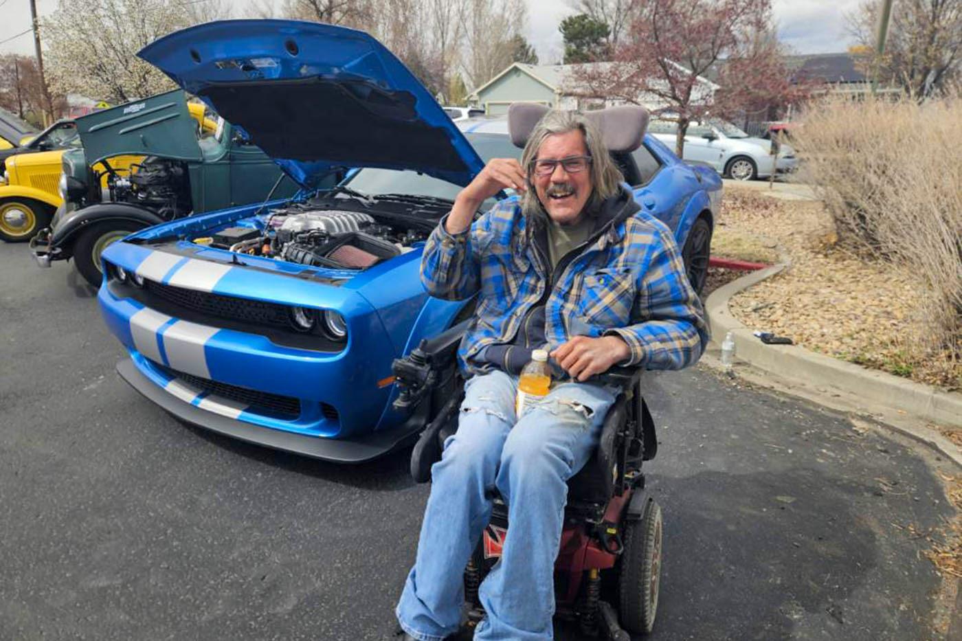 Hilltop Brain Injury Services resident smiling beside a blue classic car during a community event.